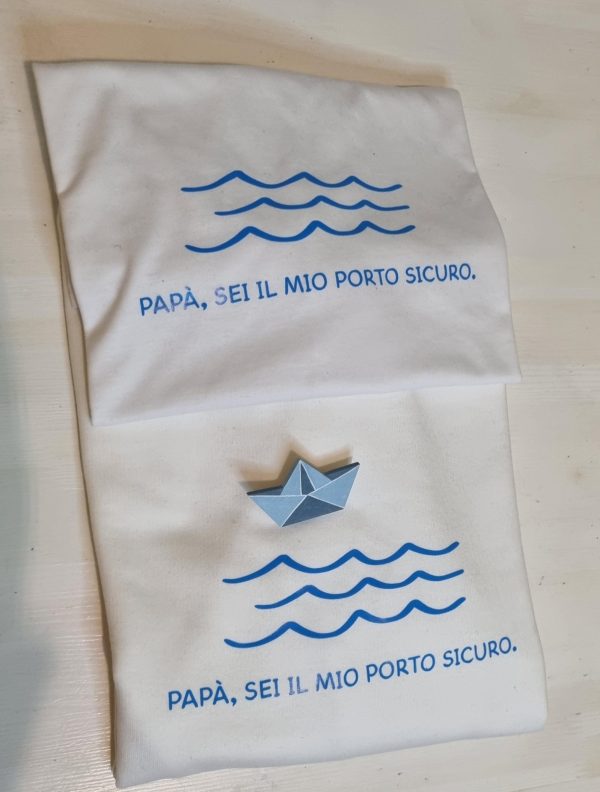 T-shirt e Felpa "Papà sei il mio porto sicuro" con spilla in legno artigianale Un regalo originale e pieno di significato per il tuo papà: t-shirt e felpa personalizzate con la frase "Papà sei il mio porto sicuro" e una spilla in legno a forma di barca, realizzata a mano. Perfette per la Festa del Papà, compleanni o qualsiasi occasione speciale, sono un modo unico per dire "grazie" a chi è sempre stato il tuo punto fermo. Qualità, creatività e tanto amore in un solo prodotto. Scopri tutte le taglie e i colori disponibili e sorprendi tuo papà con un dono unico! Tag utili felpa papà, t-shirt papà, idea regalo festa del papà, regalo originale papà, t-shirt personalizzata papà, felpa personalizzata papà, spilla barca legno, regalo emozionante papà